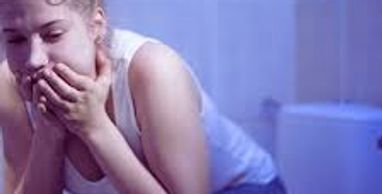 Young woman sitting on toilet looking distressed and nauseous.