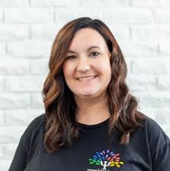 Smiling woman with wavy hair wearing a black shirt against a white brick wall.