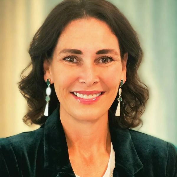 Smiling woman with curly hair wearing a dark blazer and dangling earrings.