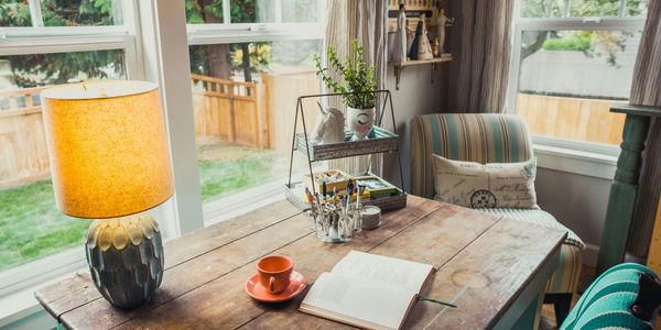 A cozy corner with a wooden table, lamp, and open book by the window.