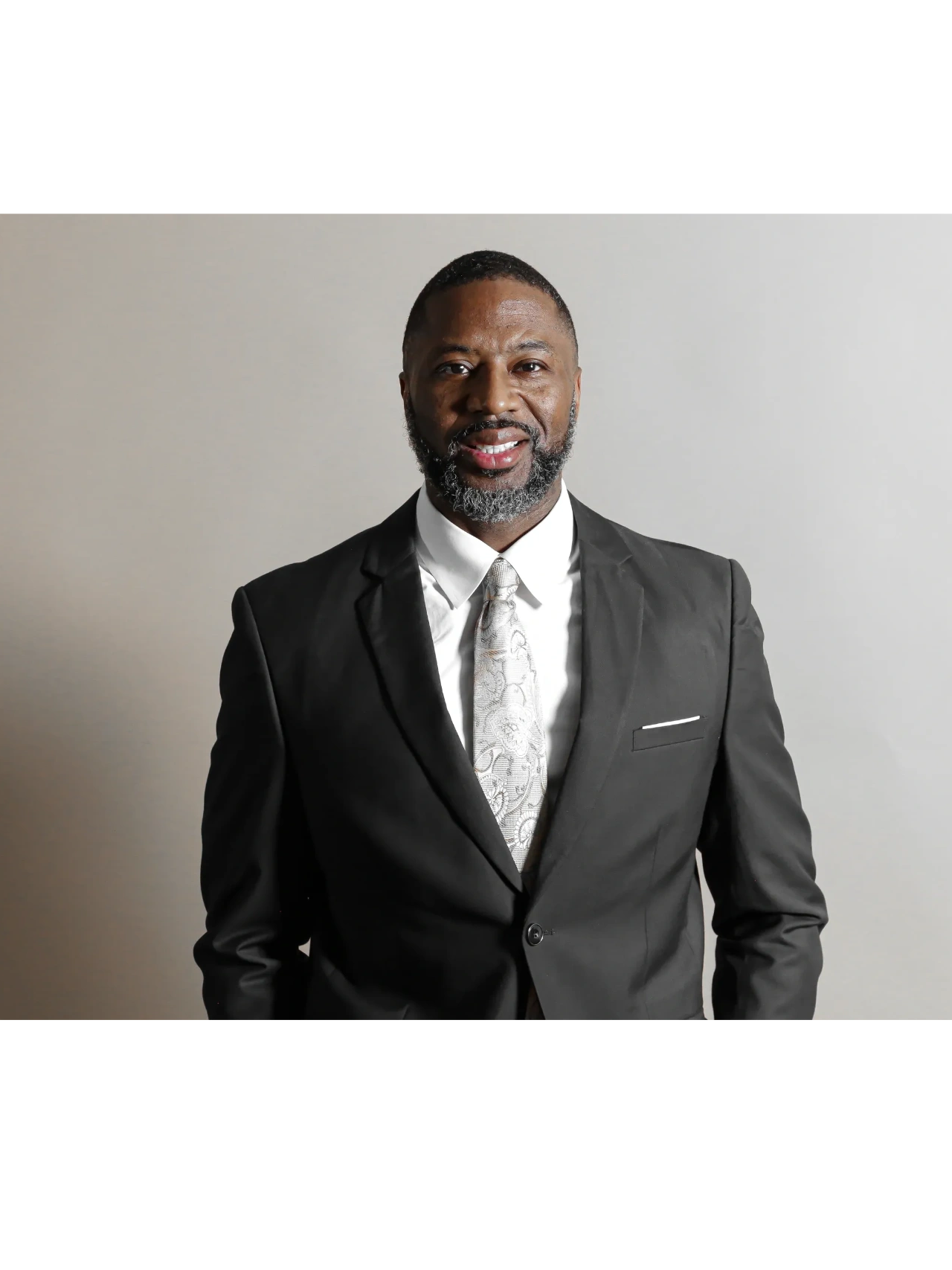 Man in a black suit with a patterned tie smiling at the camera.