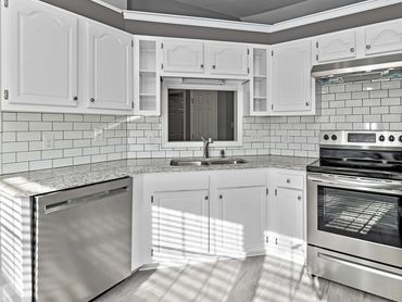 Modern kitchen with white cabinets and stainless steel appliances. We buy houses fast