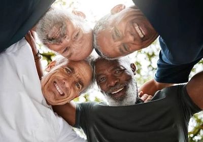 Four diverse men smiling and embracing in a circle outdoors.