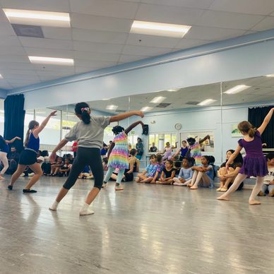 Children practicing ballet in a studio with an audience watching.
