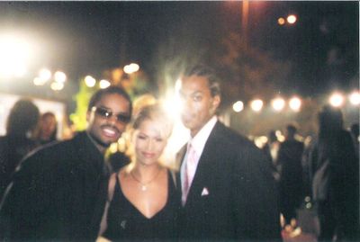 Three people dressed formally, smiling at the camera with bright lights behind them.