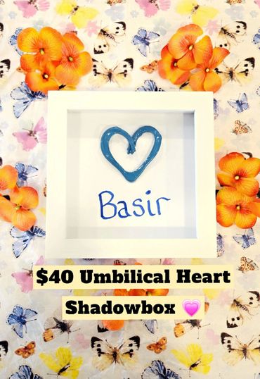 White shadowbox with blue heart and name Basir, surrounded by orange flowers on butterfly fabric.