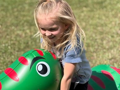 Little girl playing on a green dinosaur inflatable outdoors.