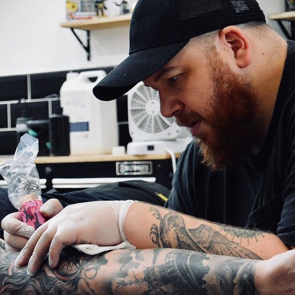 A tattoo artist intensely working on a client's arm tattoo in a studio.