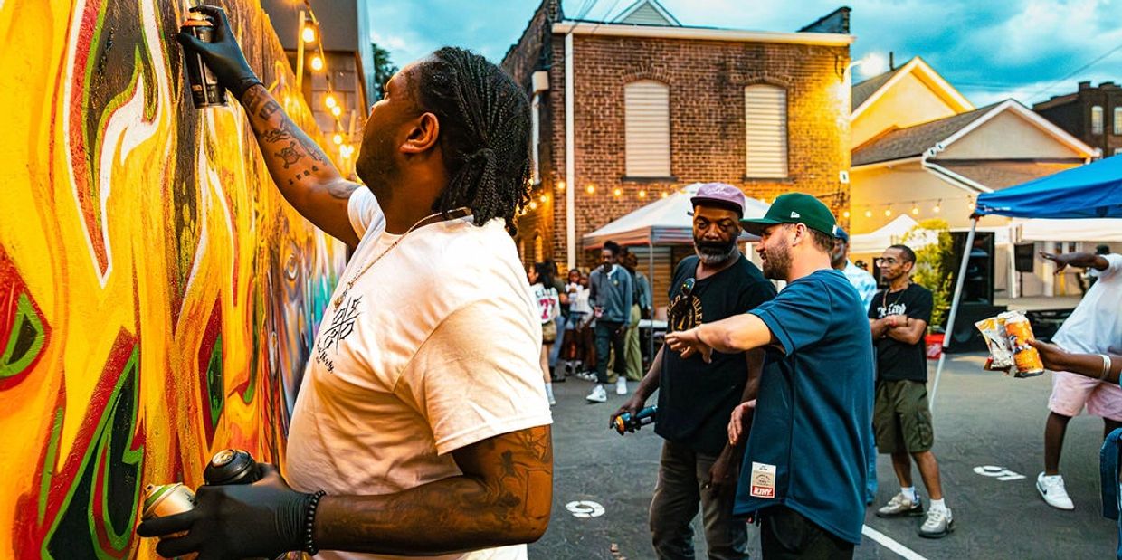 Street artist spray-painting vibrant graffiti on a wall during an outdoor event.