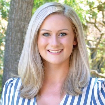 Smiling woman with blonde hair and striped top outdoors.