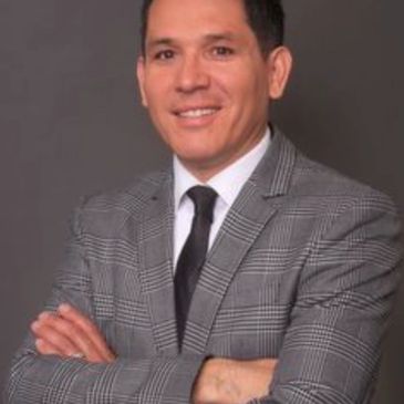 Man in a checkered suit smiling with arms crossed.