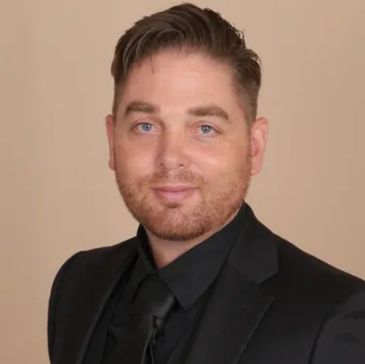 Man in a black suit with a confident smile.