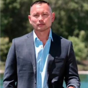 Man in a blue suit and light blue shirt outdoors.