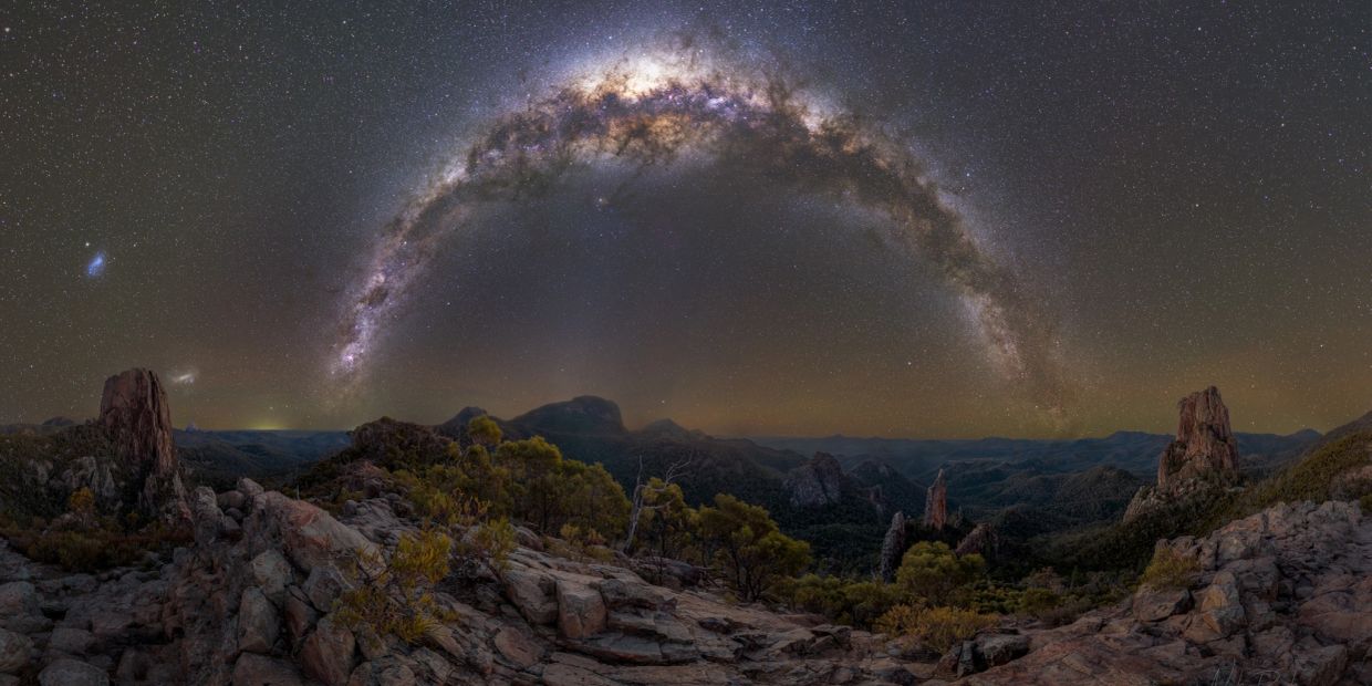Milky Way arching over rocky mountain landscape at night.