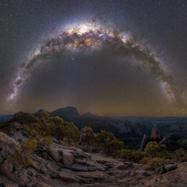 Milky Way arching over rocky terrain at night.