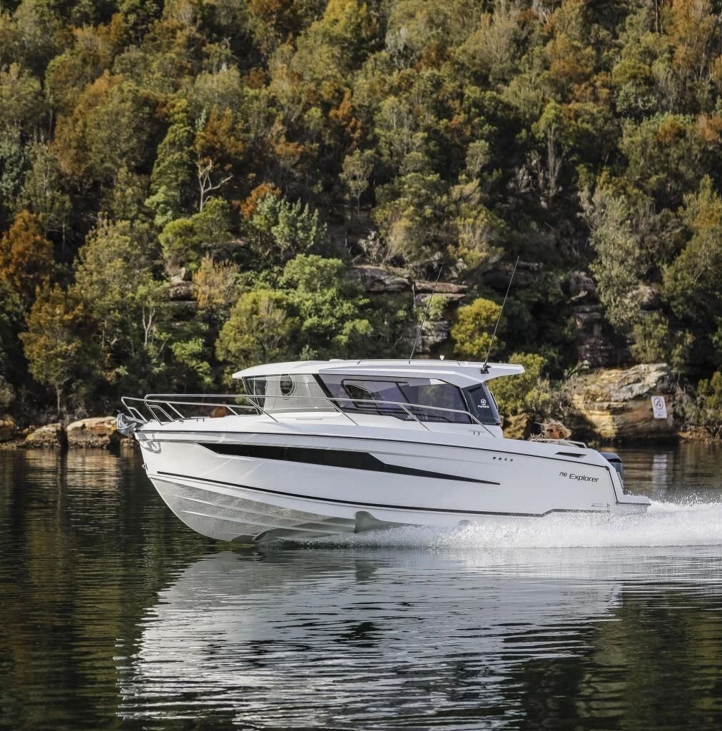A sleek white motorboat cruising on calm water near a forested shoreline.