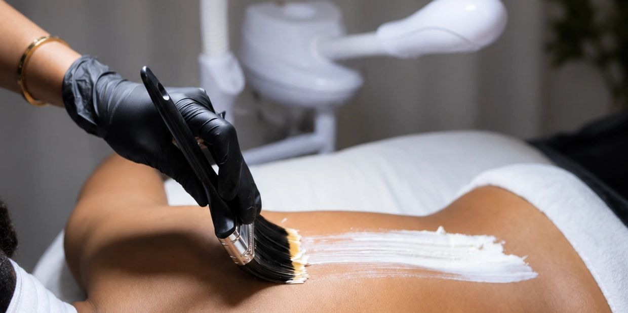 Applying a white body mask on a person's back in a spa setting.