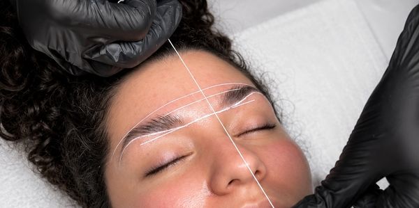 A beautician uses white thread to shape eyebrows on a woman's face.