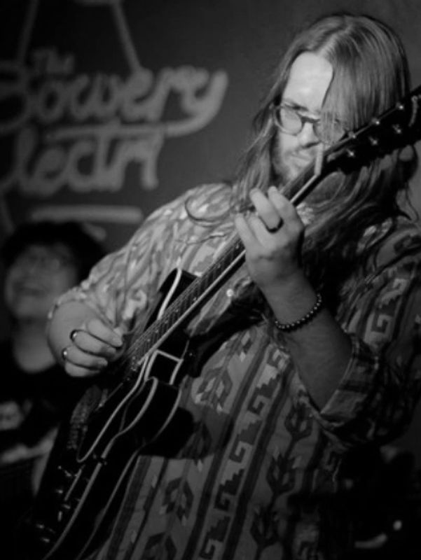 A musician passionately playing guitar on stage in a black and white photo.