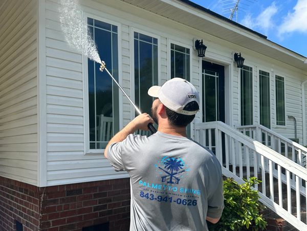 Man power washing a house exterior on a sunny day.