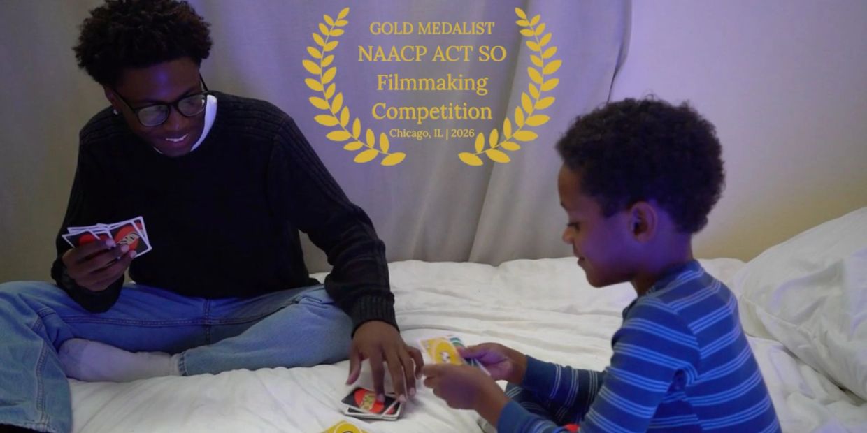 Two boys playing cards on a bed with a gold medalist award overlay.