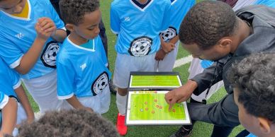 Coach discussing soccer tactics with young players using a tablet on the field.