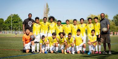 Youth soccer team in yellow jerseys posing with coaches on field.