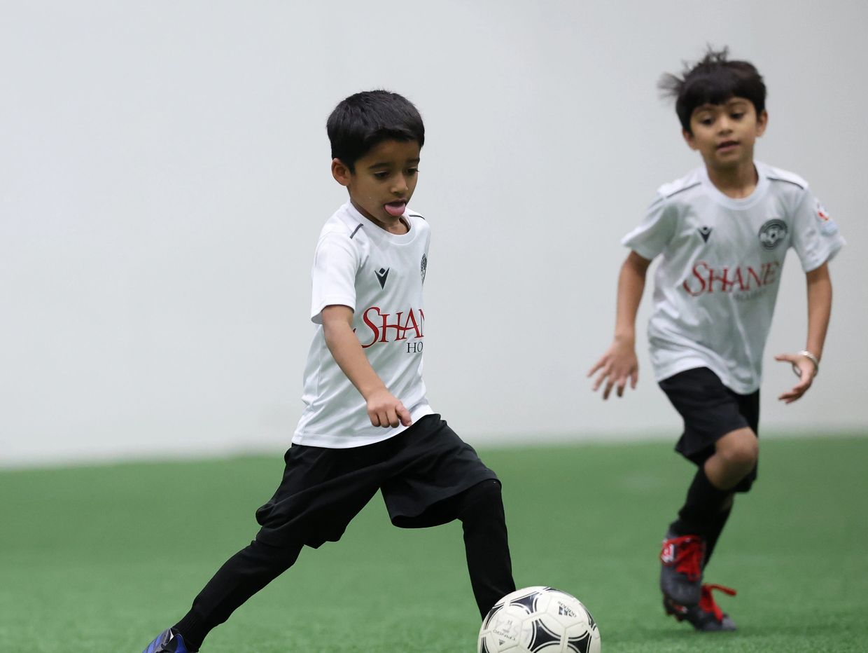 Two boys playing soccer indoors.