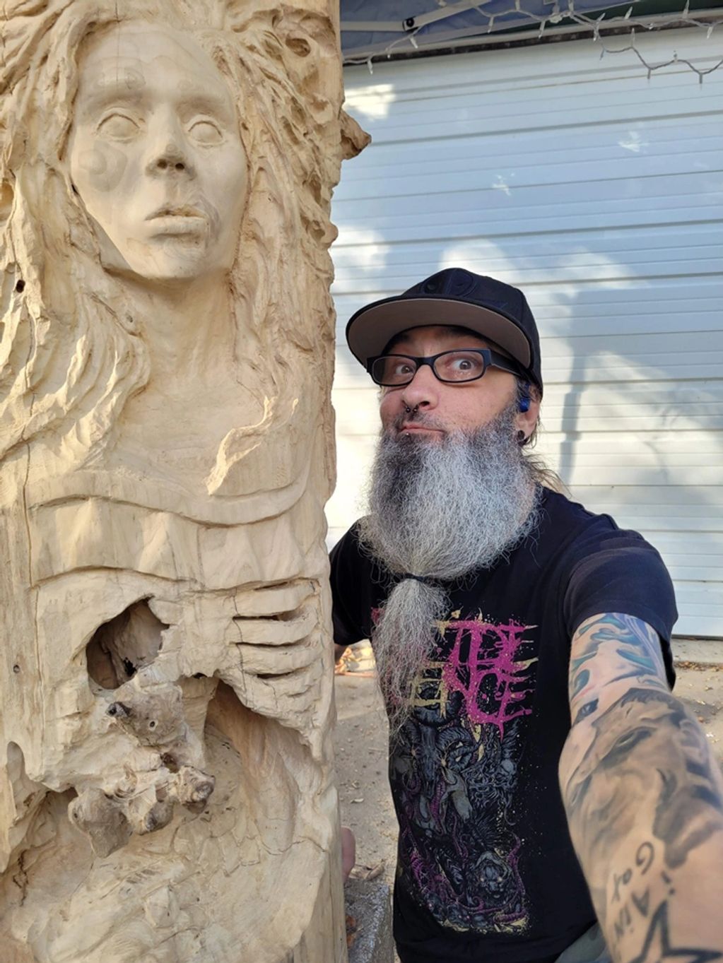 Artist Chad Rev dwarfed by a large work in progress carved from the trunk of a scarlet oak tree