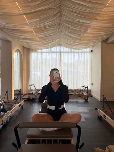 Person taking a mirror selfie while sitting cross-legged in a Pilates studio.