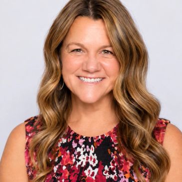 Smiling woman with wavy hair in a colorful dress.