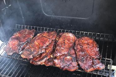 Barbecue pork steaks cooking on a smoker grill.