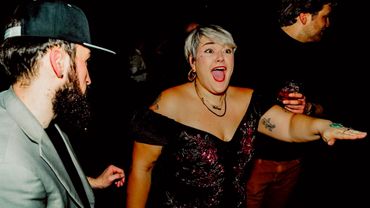 A woman excitedly dances with two men in a dark setting.