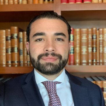 Hombre con traje y corbata frente a una estantería de libros.