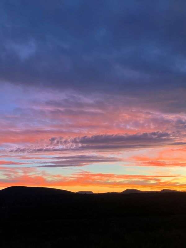 Colorful sunset over hills with dark foreground.