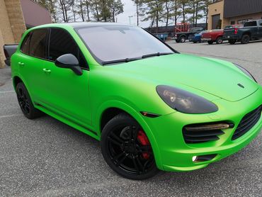 Bright green Porsche SUV with black rims parked in an industrial area.
