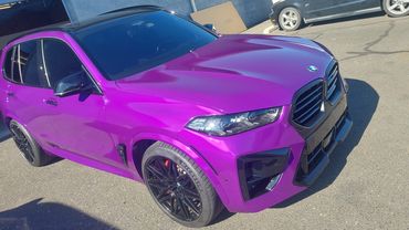 Purple BMW SUV with black rims parked outdoors on a sunny day.