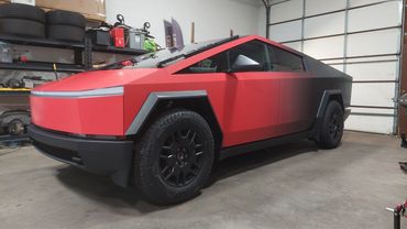 Red and black Tesla Cybertruck in a garage with black wheels and angular design.