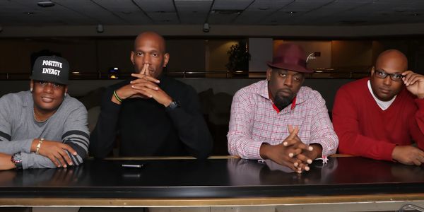 Four men sitting at a table, posing for a photo indoors.