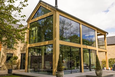 Modern house extension with large glass windows and wooden frames reflecting trees.
