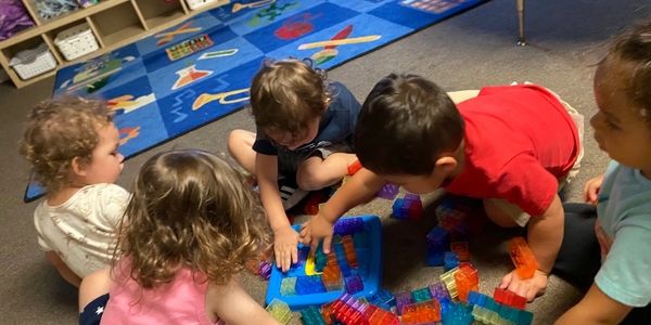 Young children playing with colorful building blocks on a carpeted floor.