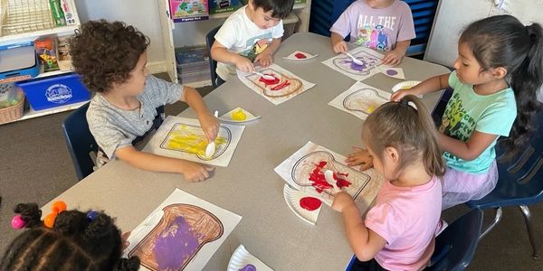 Children painting bread-shaped crafts at a classroom table.