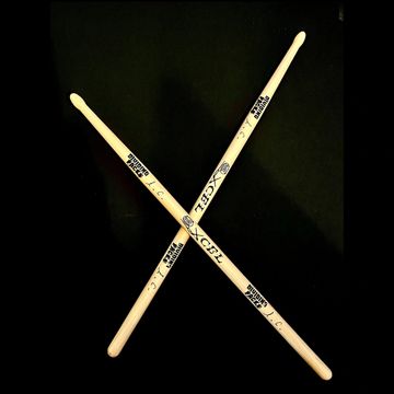 XCEL light wood drumsticks crossed over each other on a black background