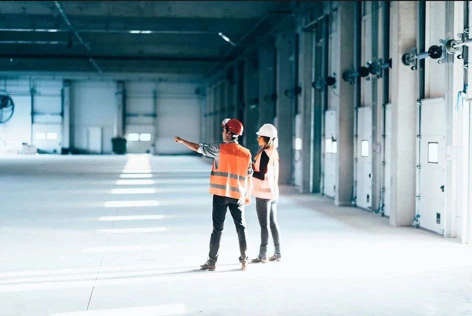 Male and female in hard hats and orange vests standing in empty warehouse