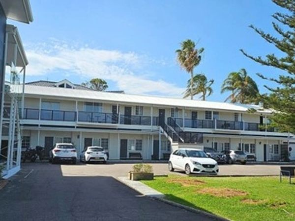 Two-story motel building with parked cars and clear blue sky.