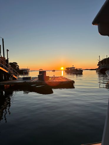 Sunset over a calm harbor with boats and a wooden dock.