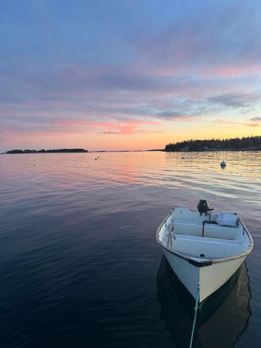 A small boat tied on calm water at sunset with a colorful sky.