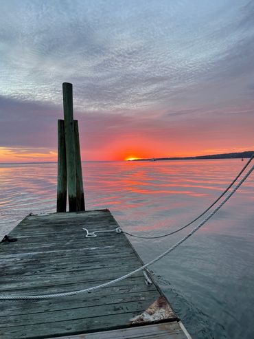 Sunset view from a wooden dock over calm water with cloudy sky.