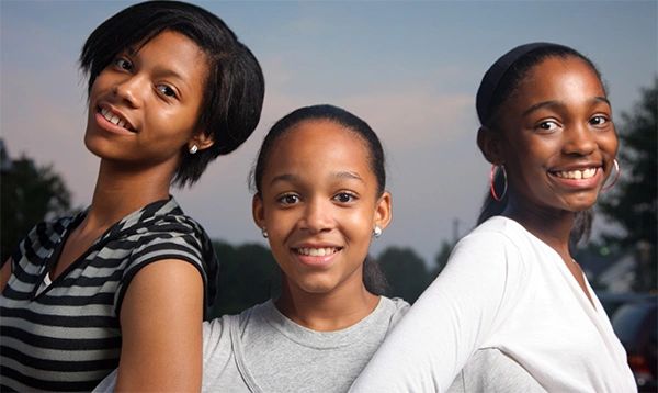 Three smiling girls posing outdoors during dusk.