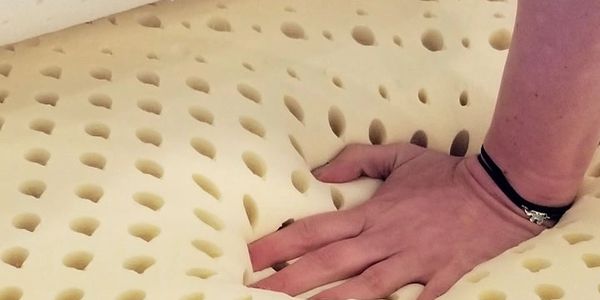 Hand pressing into a latex foam mattress showing its softness and elasticity.